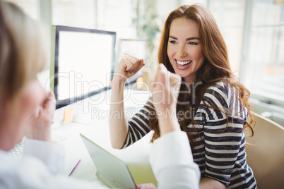 Businesswoman punching in air while discussing with colleague in