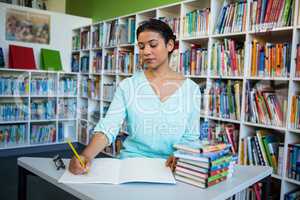 Woman writing on notebook against bookshelf in library