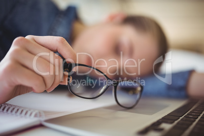 Tired businesswoman holding eyeglasses while taking nap in offic