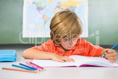 Boy writing on book in classroom