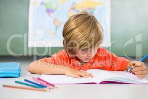 Boy writing on book in classroom