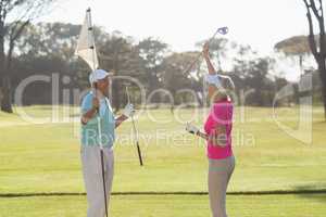 Happy mature golf player couple carrying flag