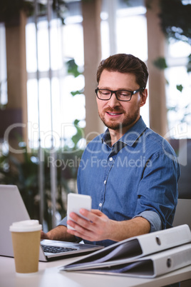 Businessman using cellphone while working on laptop at office