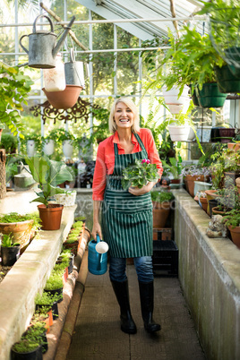Gardener with potted plant and watering can at greenhouse
