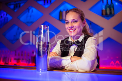 Confident barmaid sitting by cocktail shaker at counter