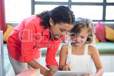 Teacher assisting girl using digital tablet in library