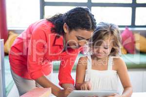 Teacher assisting girl using digital tablet in library