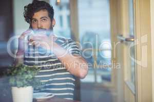 Man sipping coffee while talking on cellphone at cafe