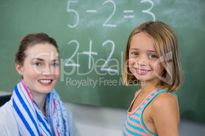Portrait of young teacher with girl in classroom