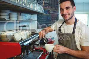 Portrait of happy barista pouring coffee at cafe