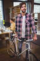 Creative businessman standing by bicycle in office