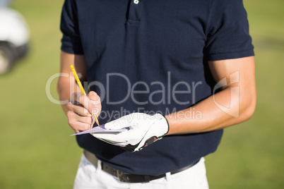 Midsection of golfer writing on score card