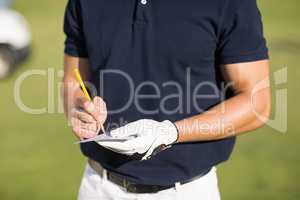 Midsection of golfer writing on score card