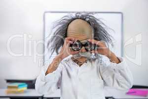 Boy dressed as scientist holding eyeglasses in classroom