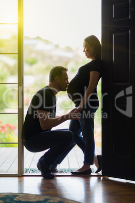 Husband Kissing Belly of Pregnant Wife Silhouetted In Doorway.