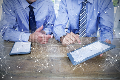 Composite image of businessmen using digital tablet at table