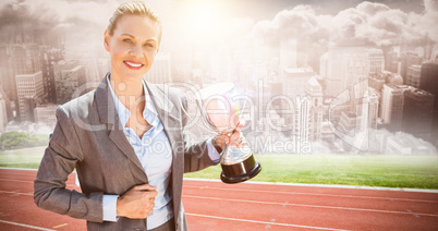 Composite image of successful businesswoman holding a trophy