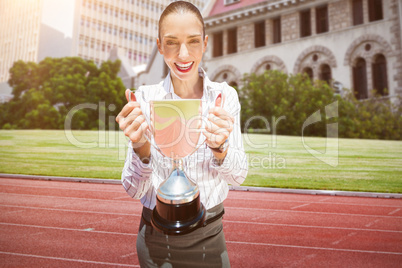 Composite image of successful businesswoman holding a trophy