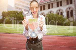 Composite image of successful businesswoman holding a trophy