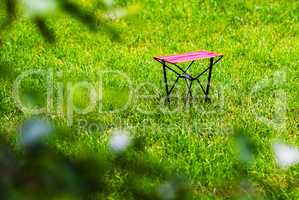 Horizontal vivid red chair on green grass bokeh background