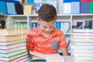 Schoolboy sitting on table and reading book in library