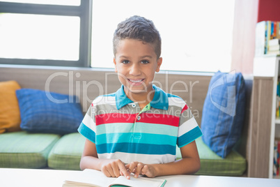 Schoolboy sitting on table and reading book in library