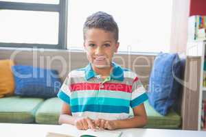 Schoolboy sitting on table and reading book in library