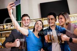Young friends taking selfie while holding beer mug