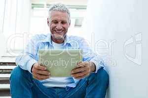 Smiling mature man holding tablet while sitting on steps