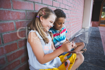 Schoolkids sitting in corridor and using digital tablets