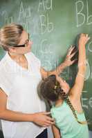 Teacher assisting schoolgirl to learn alphabet on chalkboard in