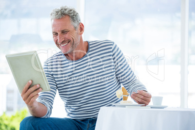 Smiling mature man holding digital tablet while having food