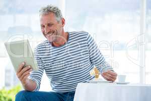 Smiling mature man holding digital tablet while having food