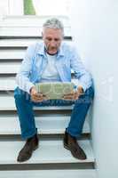 Mature man holding tablet while sitting on steps