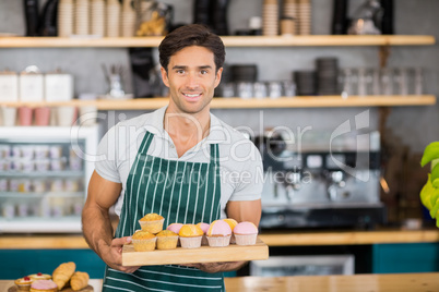 Portrait of smiling waiter holding a tray of cupcakes