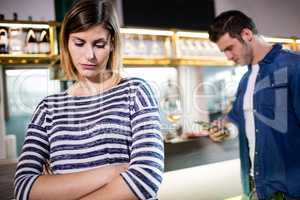 Woman with arms crossed while boyfriend using cellphone