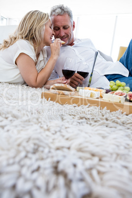 Woman feeding food to man while lying on rug