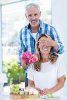 Man covering eyes of wife while giving roses