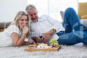 Happy couple with red wine and food while lying on rug