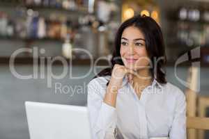 Thoughtful businesswoman sitting on table with laptop