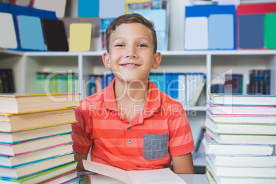 Schoolboy sitting on table and reading book in library