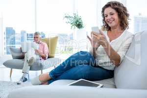 Smiling woman using smartphone by man sitting at home