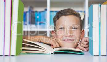 Schoolboy sitting on table and reading book in library