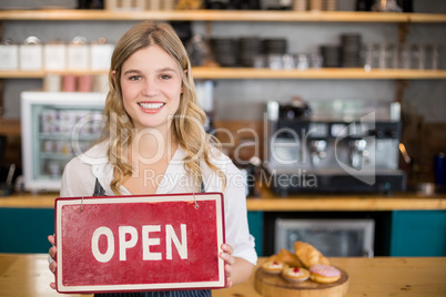 Smiling waitress showing signboard with open sign at cafe