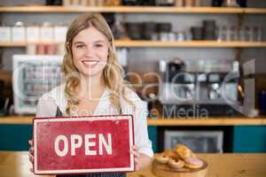 Smiling waitress showing signboard with open sign at cafe