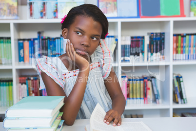 Schoolgirl sitting on table and reading book in library