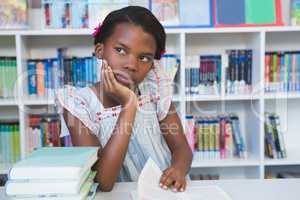 Schoolgirl sitting on table and reading book in library