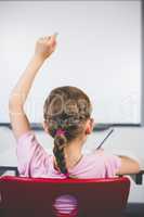 Rear view of schoolgirl raising her hand in classroom