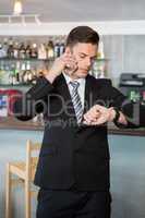 Businessman checking time while talking on the mobile phone