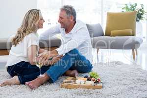 Romantic couple with white wine and food while sitting on rug